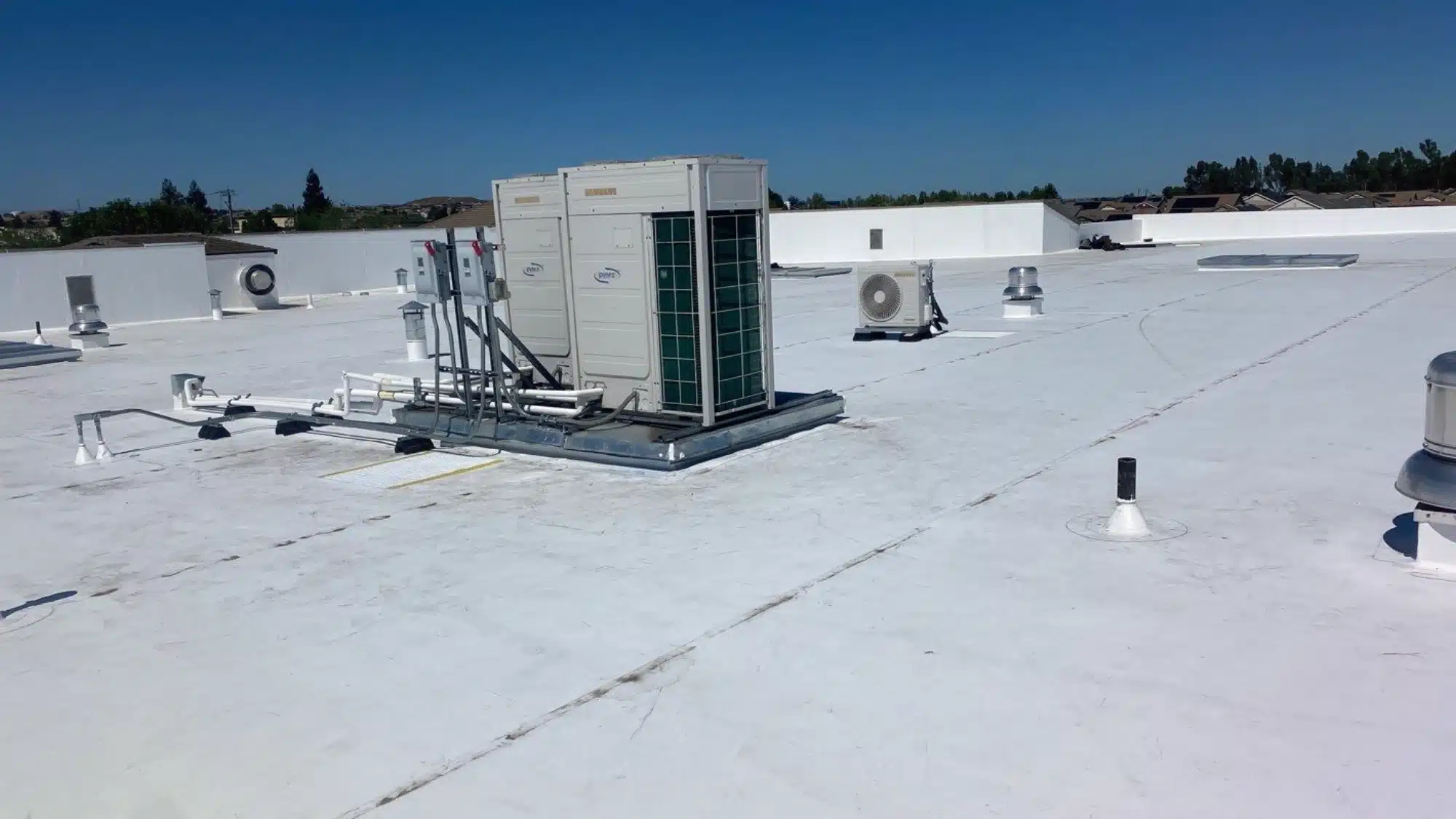 Commercial roofing inspector examining flat roof system including drainage, membrane condition, flashing, and HVAC rooftop units on a business building