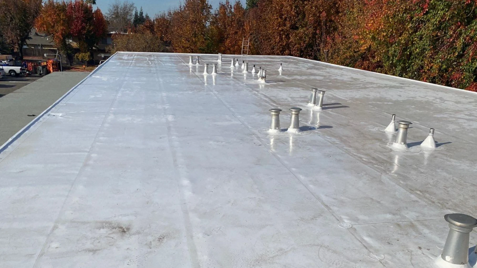 A professional applies a durable, light-colored coating to a commercial building roof, improving its longevity and appearance.