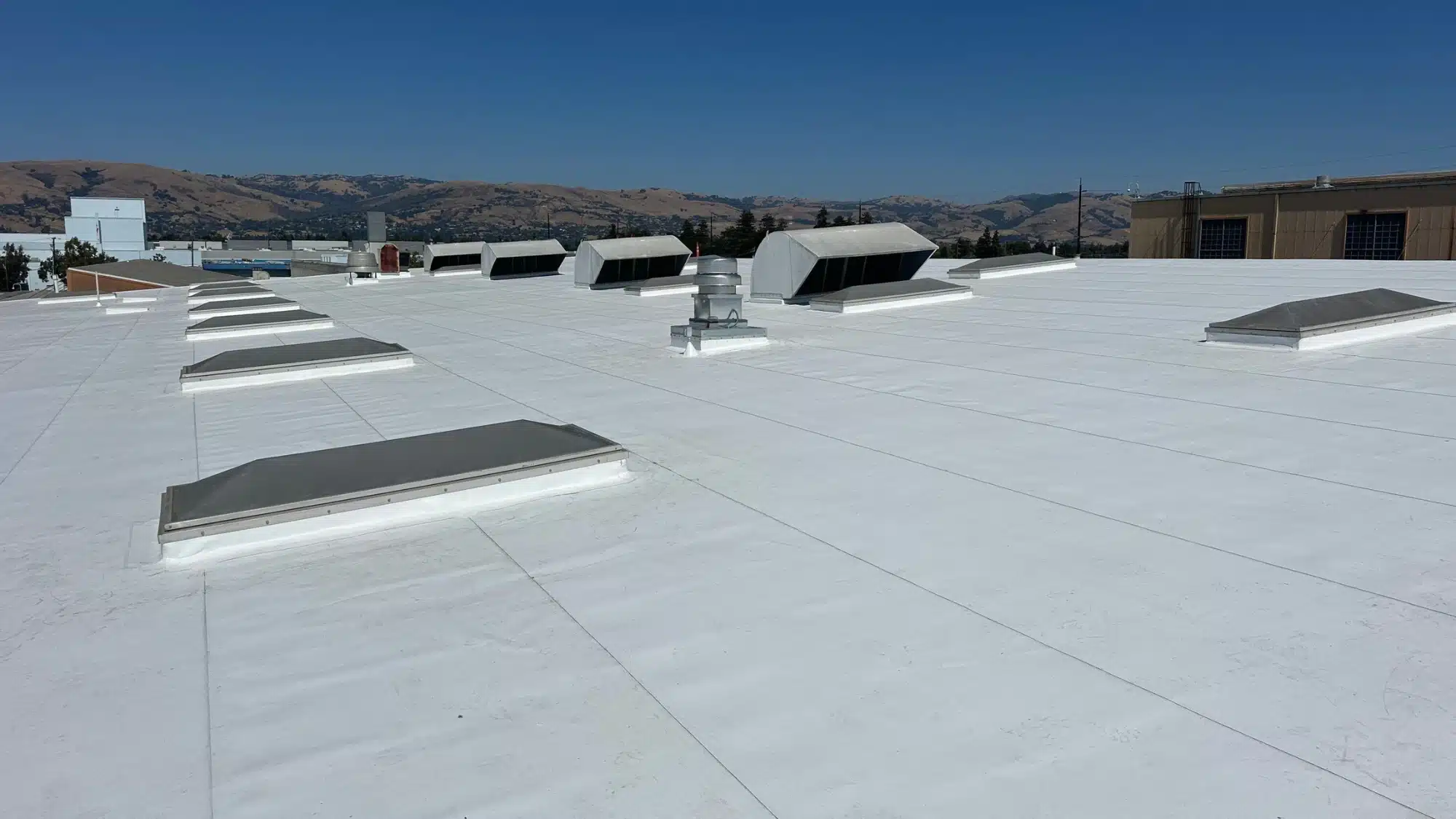 White roof coating system applied to a flat commercial roof with skylights and ventilation equipment for long-lasting protection and energy efficiency.