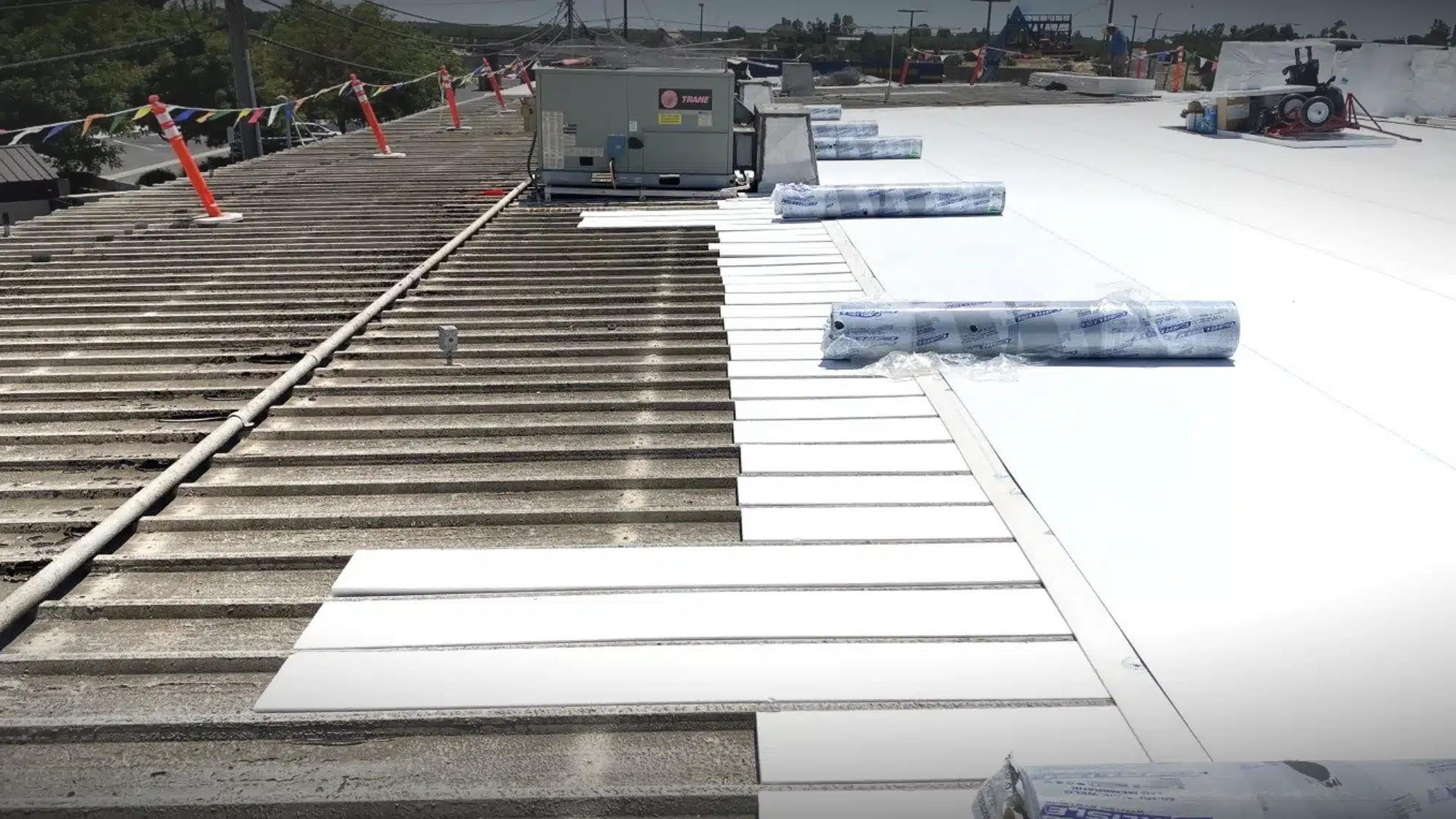 Commercial roofing installation showing a white membrane roofing system being applied over an existing industrial roof.